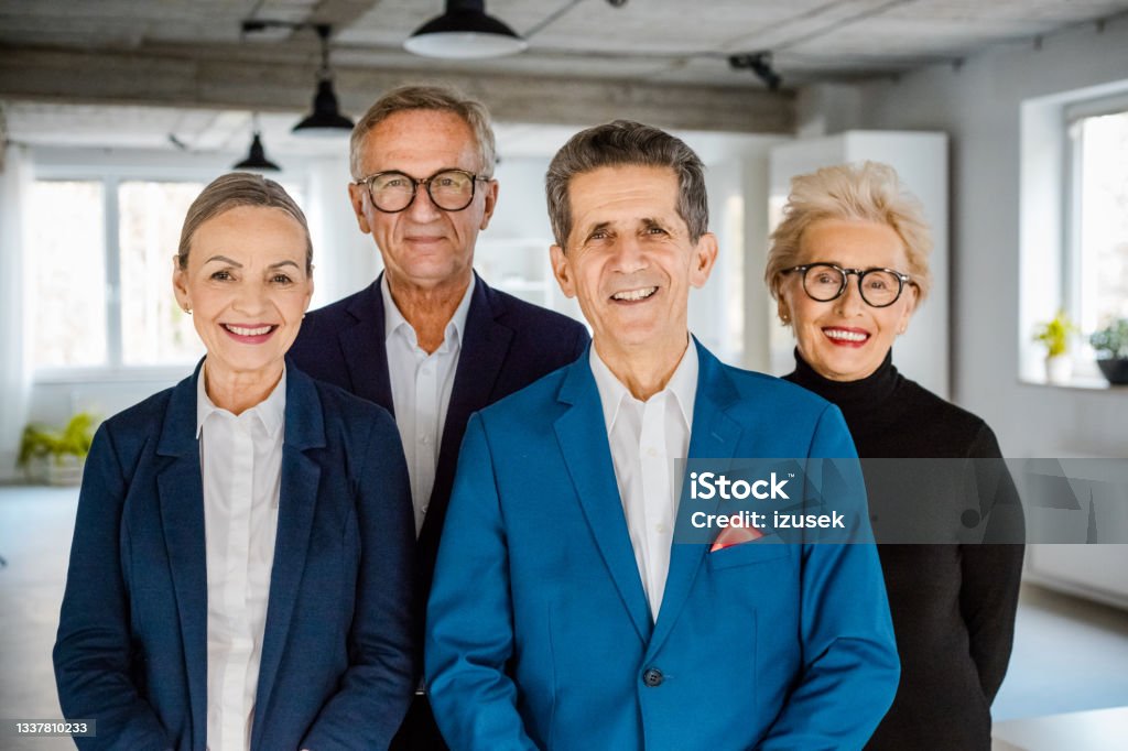 Successful business senior people Portrait of senior businesswomen and businessmen wearing elegant suits standing in the modern office and smiling at camera. Business Person Stock Photo
