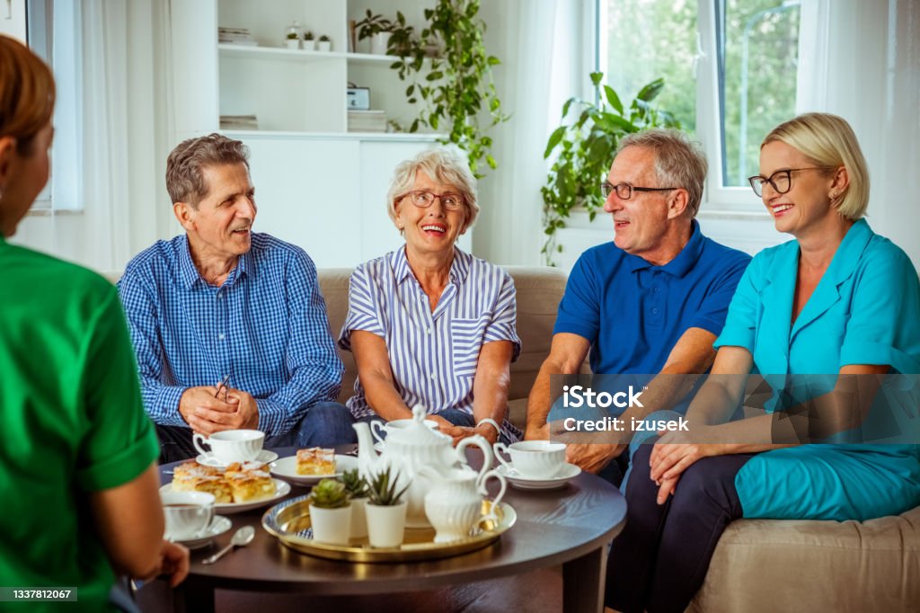Cheerful senior people in retirement house Happy senior women and man spending time together in nursing home, talking with female social worker and nurse, drinking coffee. Assisted Living Stock Photo