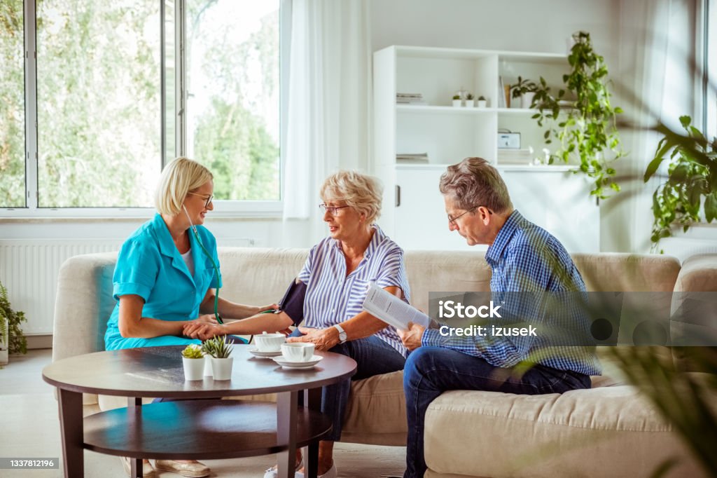 Elderly lady talking with nurse Nurse measuring blood pressure of senior woman. They are sitting with nurse in hospital waiting room. Emotional Stress Stock Photo