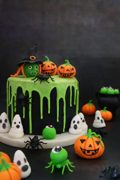 Stock photo showing a close-up view of homemade layered sponge cake decorated with black fondant and dripping, green glace icing to celebrate Halloween.