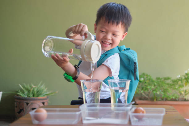criança asiática feliz estudando ciência, derramando água para fazer divertido e fácil experimento de ciência de ovos flutuantes - fun simplicity children only color image - fotografias e filmes do acervo