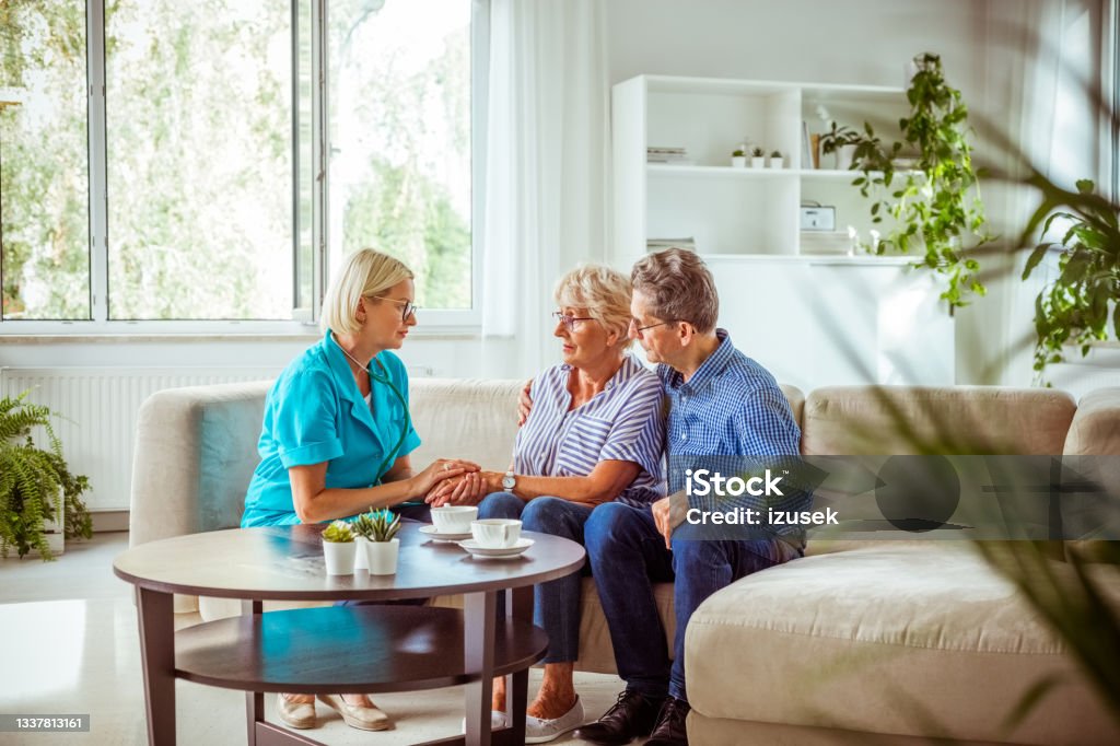 Worried senior couple talking with nurse Worried senior woman feeling unwell, getting bad news. Senior man consoling his wife. They are sitting with nurse in hospital waiting room. 70-79 Years Stock Photo