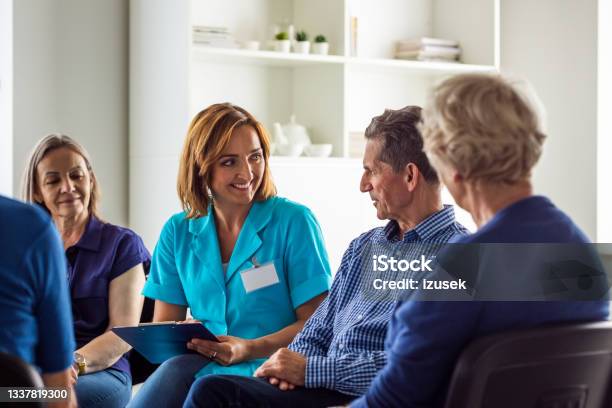 Cheeful Nurse During Meeting With Senior People Stock Photo - Download Image Now - Nursing Home, Hospital, Social Worker