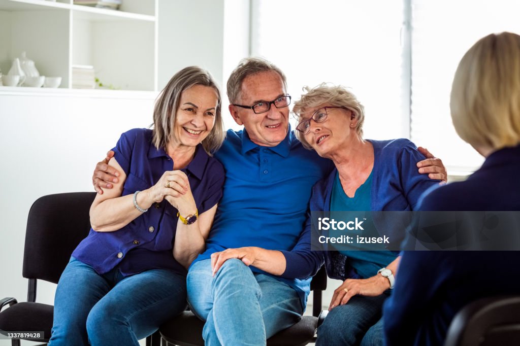 Cheerful senior people during group therapy Happy senior people sharing issues with patients during meeting in nursing home. Senior man embracing elderly ladies. Happiness Stock Photo