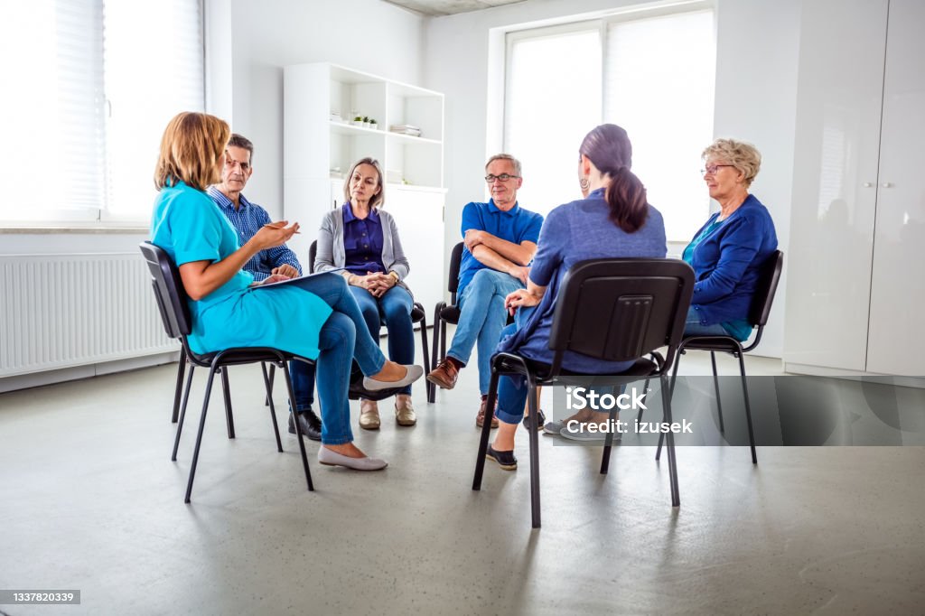 Nurse during meeting with senior people in nursing home Nurse taking with senior people during meeting in nursing home. They are discussing about mental wellbeing. Hospital Stock Photo