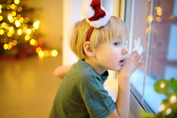 małe podekscytowane dziecko czeka na świętego mikołaja w wigilię. przedszkolak patrzący na okno i nadzieja na magię i prezenty w noc sylwestrową. - christmas window magic house zdjęcia i obrazy z banku zdjęć