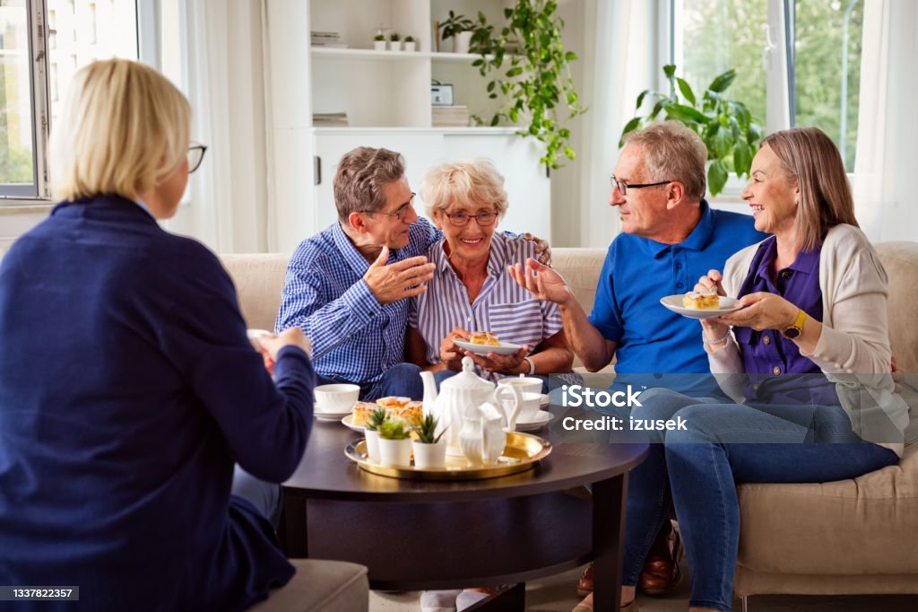 Cheerful senior people in retirement house Happy senior women and man spending time together in nursing home, talking with female social worker, drinking coffee, eating cakes. 70-79 Years Stock Photo