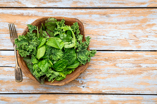 Top view of bowl with green fresh baby spinach on grey concrete background