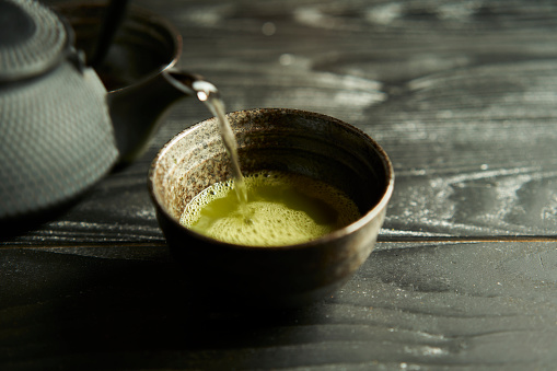 Japanese organic matcha green tea in cup on black wood background.