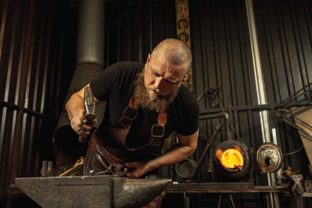 istock Bearded man, blacksmith manually forging the molten metal on the anvil in smithy with spark fireworks. Concept of labor, retro professions, family business 1337829414