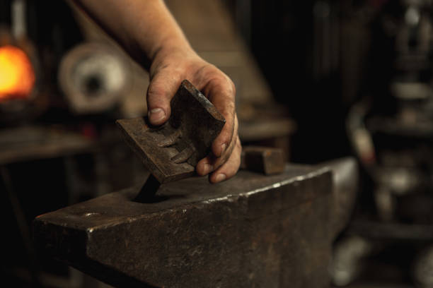 Hard work. Energy and power. Close-up working powerful hands of male blacksmith forge an iron product in a blacksmith. Hammer, red hot metal and anvil. Concept of labor, retro professions