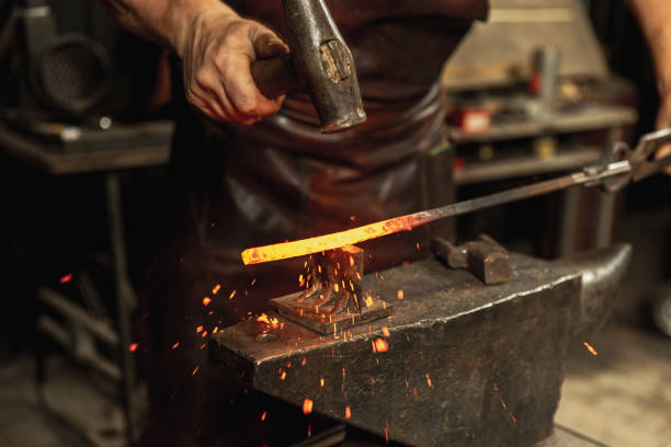 istock Close-up working powerful hands of male blacksmith forge an iron product in a blacksmith. Hammer, red hot metal and anvil. Concept of labor, retro professions 1337829431