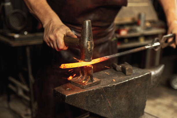 istock Close-up working powerful hands of male blacksmith forge an iron product in a blacksmith. Hammer, red hot metal and anvil. Concept of labor, retro professions 1337829436
