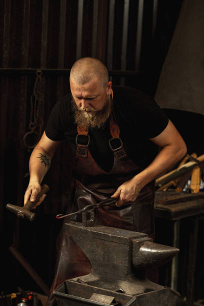 istock Bearded man, blacksmith manually forging the molten metal on the anvil in smithy with spark fireworks. Concept of labor, retro professions, family business 1337829446