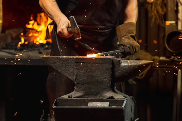 istock Bearded man, blacksmith manually forging the molten metal on the anvil in smithy with spark fireworks. Concept of labor, retro professions, family business 1337829481
