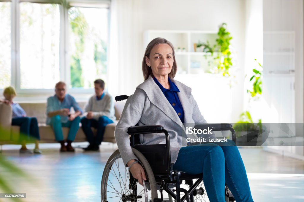 Elderly lady in wheelchair Elderly lady sitting in wheelchair. Smiling senior woman in retirement house. Parkinson's Disease Stock Photo