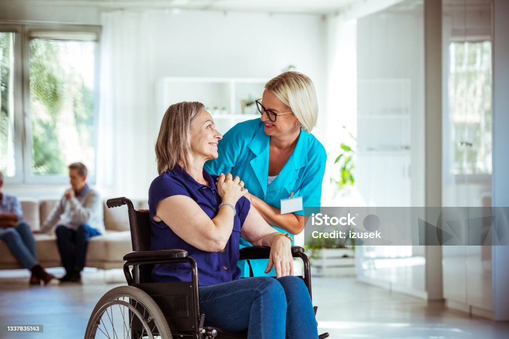 Friendly nurse consoling senior woman Home nurse holding hands of worried senior woman in retirement house. Elderly lady sitting in wheelchair. Social Services Stock Photo