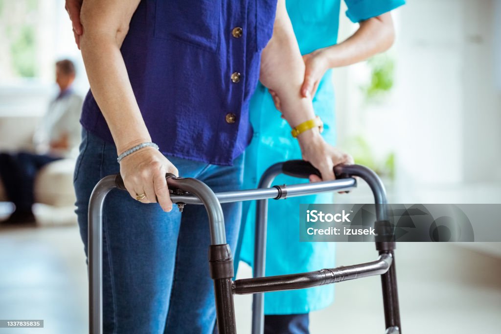 Nurse helping senior woman to use walking frame People in nursing home. Nurse wearing uniform helping elderly lady to use walking frame. Close up of hands, unrecognizable people. Parkinson's Disease Stock Photo
