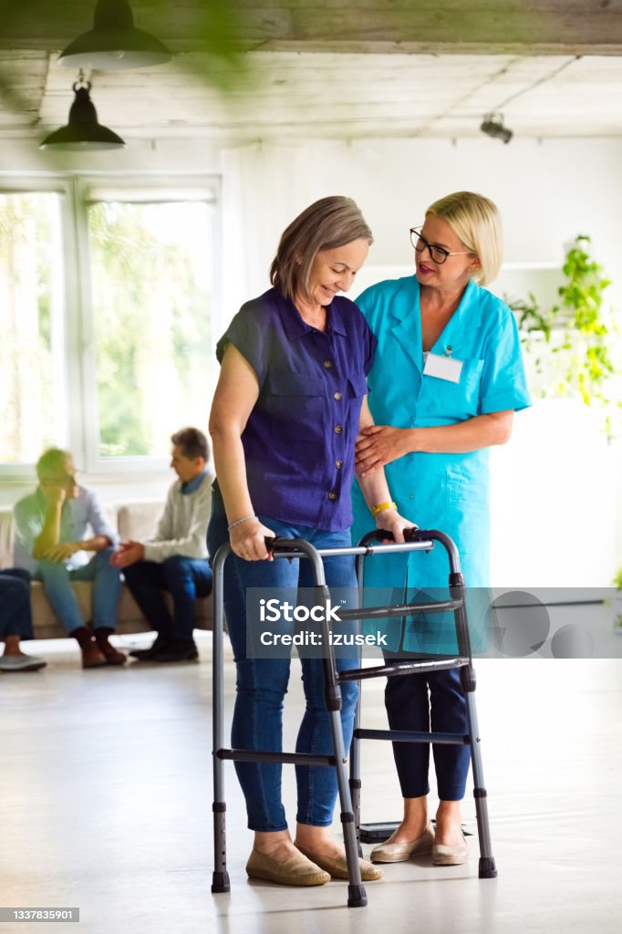 Nurse helping senior woman to use walking frame People in nursing home. Friendly nurse wearing uniform helping elderly lady to use walking frame. Parkinson's Disease Stock Photo