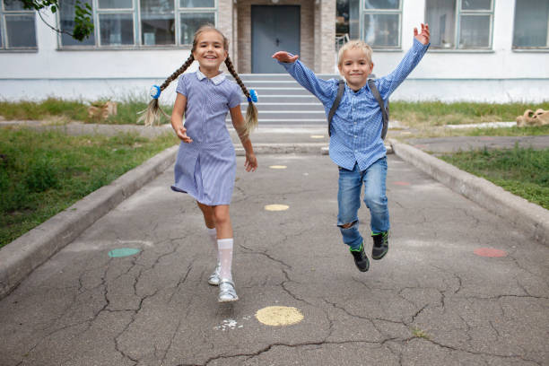 istock Back to school. Siblings with backpacks running from the school after their first offline day 1337839057