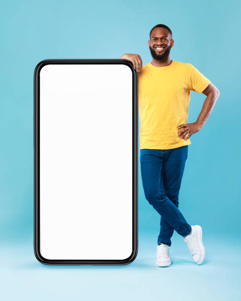 istock Cheerful Afro guy leaning on giant smartphone, demonstrating empty screen, space for online ad, mockup for mobile app 1337841002