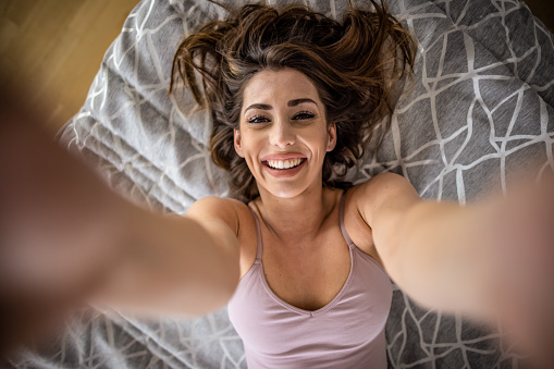 Photo of beautiful young woman lying on bed and taking selfie with smart phone