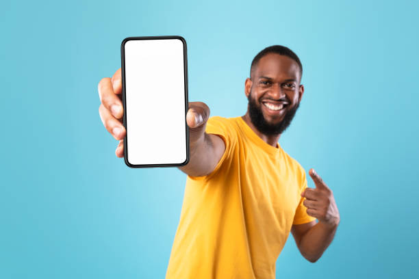 istock Excited black guy pointing at cellphone with empty screen on blue background, mockup for website or mobile app 1337841438