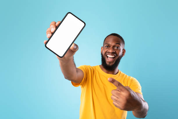 istock New awesome mobile app. Black guy pointing at smartphone with blank screen on blue background, mockup 1337841476