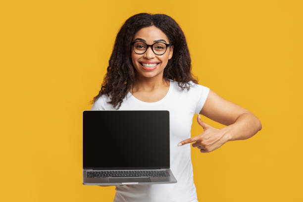 istock Online education. Happy black female student pointing at laptop with empty screen and smiling on yellow background 1337841548