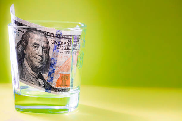 istock 100 dollar bill in whiskey glass on green background 1337841638