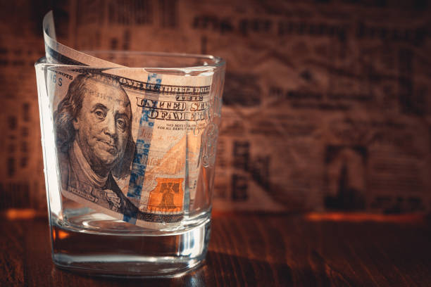 istock 100 dollar bill in whiskey glass on newspaper background 1337841686