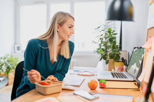 Young woman eating lunch while working from home office stock photo