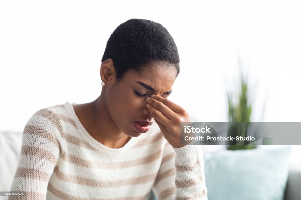 Sinusitis Concept. Sick Young Black Woman Touching Her Nose Bridge At Home Sinusitis Concept. Sick Young Black Woman Touching Her Nose Bridge While Sitting On Couch At Home, African American Lady Feeling Unwell, Suffering From Rhinitis Or Seasonal Allergy, Free Space Emotional Stress Stock Photo