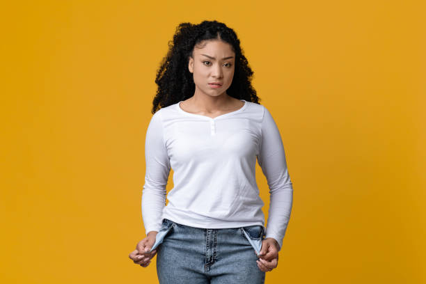 Poverty Concept. Portrait Of Upset Young Black Woman Showing Her Empty Pockets Poverty Concept. Portrait Of Upset Young Black Woman Showing Her Empty Pockets And Looking At Camera, Broke Poor Millennial African American Lady Standing Over Yellow Studio Background, Copy Space begging currency beggar poverty stock pictures, royalty-free photos & images