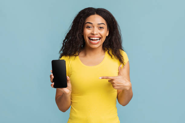 istock Overjoyed african american lady pointing at modern smartphone empty blank screen over blue background 1337850690