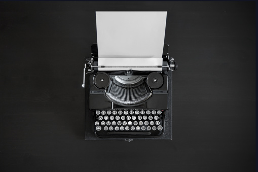 Antique black typewriter with an empty white document clamped in place on a black desk - view from above