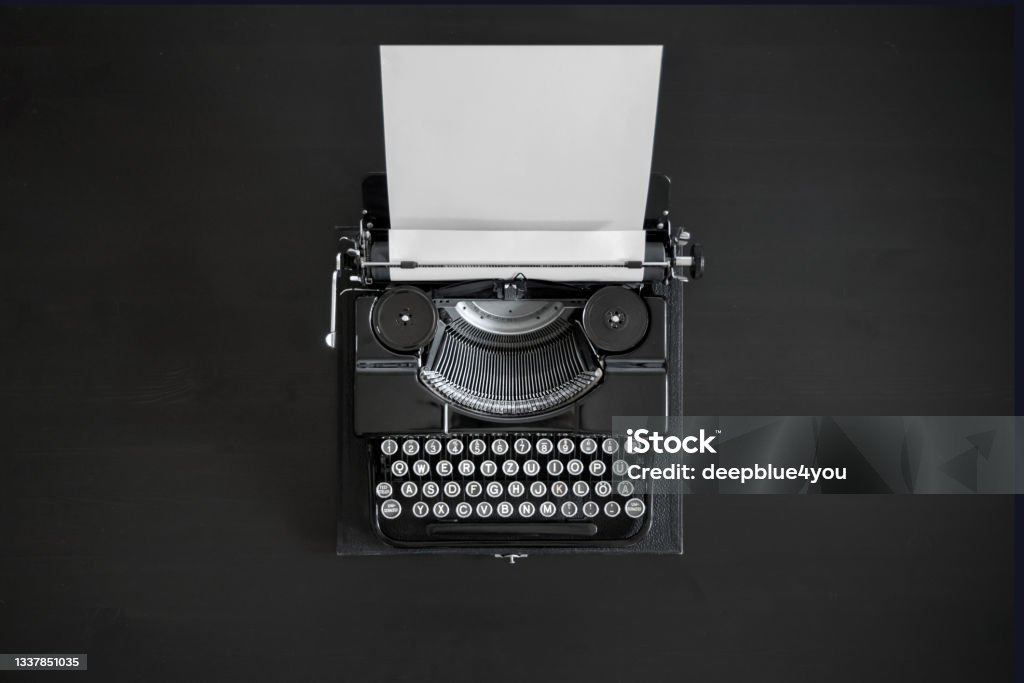 Black typewriter with an empty white document on black desktop Antique black typewriter with an empty white document clamped in place on a black desk - view from above Old-fashioned Stock Photo