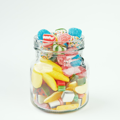 Assorted candies in a glass jar on a white background.