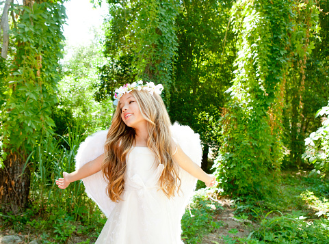 Angel children girl open arms in forest with white wings and flowers crown