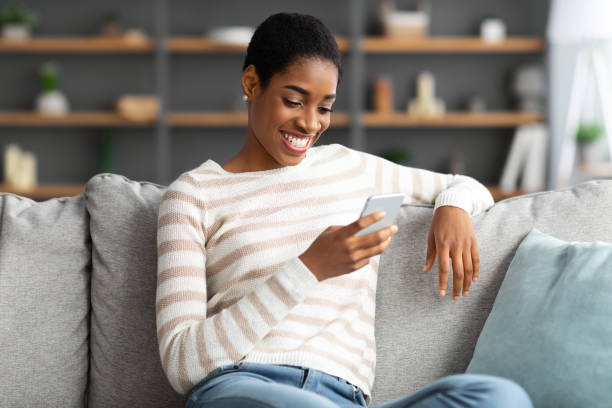 istock Smiling Black Woman Browsing New App On Smartphone While Resting At Home 1337854199