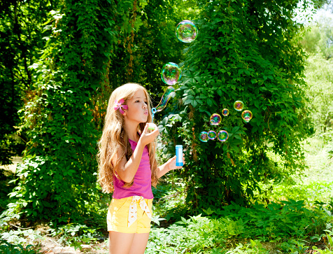 Children girl blowing soap bubbles in outdoor forest