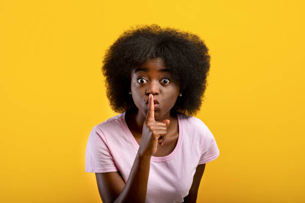 istock Keep silence. Black lady showing shh gesture at camera, stanfing over yellow background, studio shot 1337854884