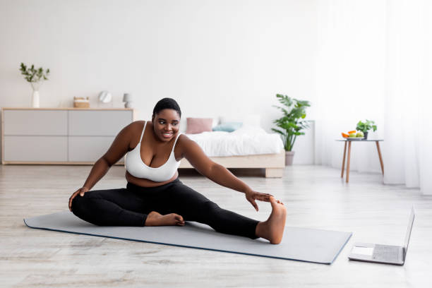 istock Plump black lady stretching legs, practicing yoga on mat, following tutorial on laptop, doing exercises online at home 1337856813