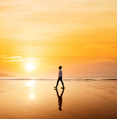 Woman walking on wet sand at sunset.