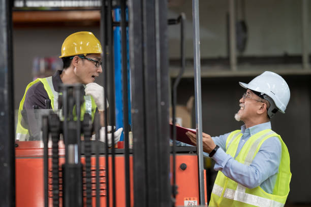 istock Asian Chinese warehouse supervisor manager signing documents receiving goods from his coworker operating forklift working in industry factory 1337862526