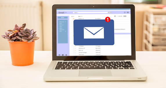 Email message inbox on computer laptop screen on a white office desk, blur room interior background.