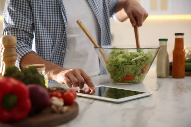 istock Man with tablet cooking salad at table in kitchen, closeup 1337870376
