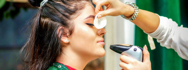 istock Side view of a make-up artist using aerograph making an airbrush makeup foundation on a female face in a beauty salon. 1337877120
