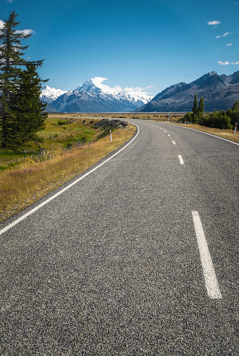 A curving road leading towards the snow covered peak of Aoraki, New Zealand's tallest mountain, also known as Mount Cook.