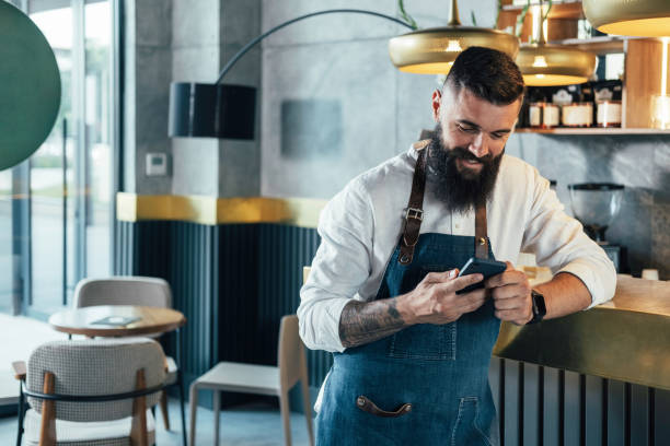 barista feliz usando el teléfono móvil en un café - waiter fotografías e imágenes de stock